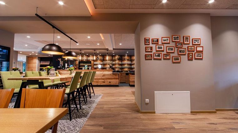 Ein modernes Restaurant mit Holzfußboden und eleganten Möbeln. An der Wand hängen Bilderrahmen mit Fotos, während die Bar im Hintergrund gut beleuchtet ist.