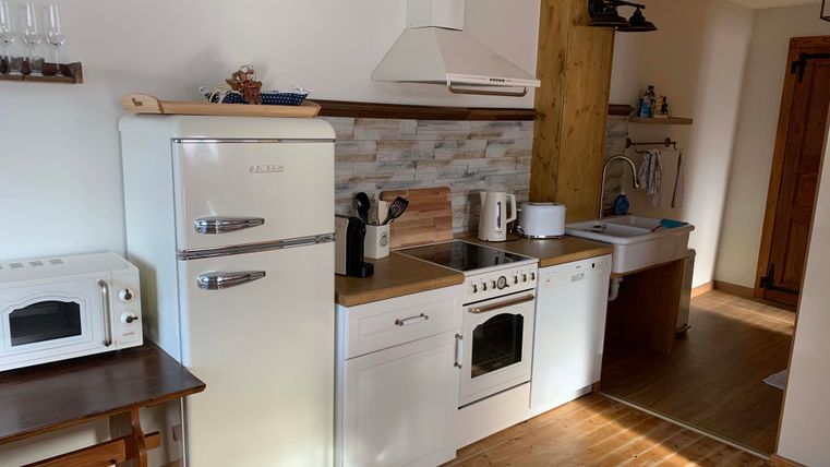 A modern kitchen with white furniture and wooden flooring. The equipment includes a refrigerator, stove, and sink.