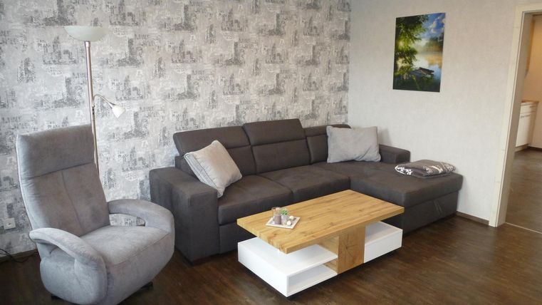 A modern living room with a gray sofa and a beige armchair. The wooden table in the middle complements the cozy atmosphere.