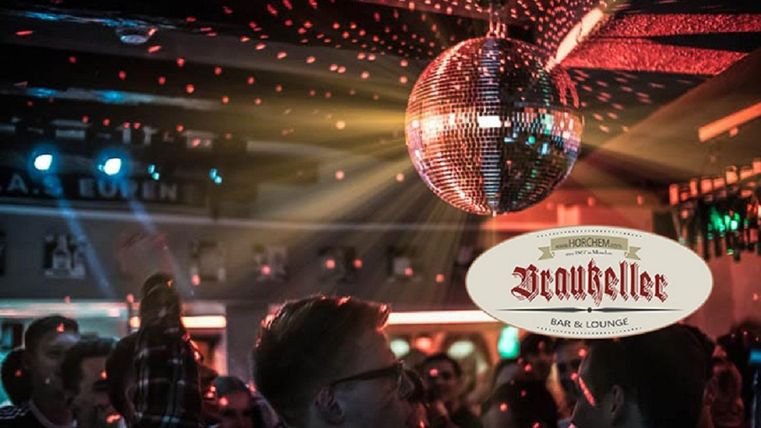 A lively bar with dancing people and a sparkling disco ball. Colorful lights create a festive atmosphere.