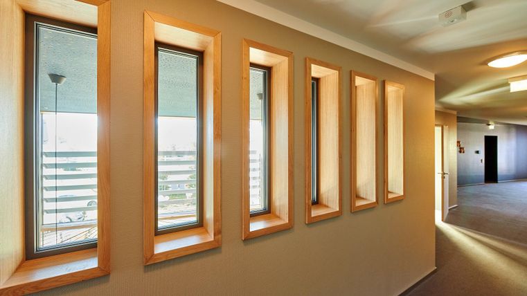 Ein heller Flur mit mehreren schmalen Fenstern, die viel Tageslicht hereinlassen. Die Wände sind in neutralen Farben gehalten und sorgen für eine moderne Atmosphäre.