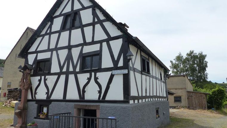 Ein traditionelles Fachwerkhaus mit weißen Wänden und schwarzen Balken. Es liegt in einer ruhigen Umgebung, umgeben von Natur.