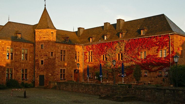 Ein historisches Schloss aus rotem Stein mit einem markanten Turm. Die Fassade ist mit lebendigen Farben geschmückt, die der Architektur einen besonderen Charme verleihen.