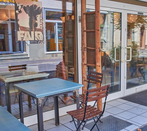 An inviting café with blue tables and a wooden bench in front of the entrance door. The colorful design creates a cozy atmosphere.