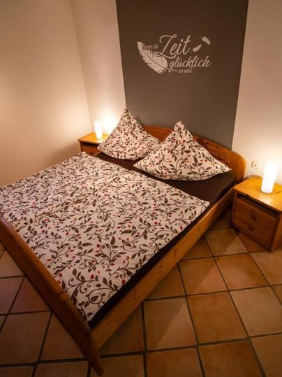 A cozy bedroom with a wooden bed and colorful cushions. Next to the bed are nightstands with stylish lamps.
