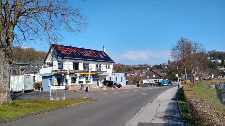 A street next to a river with a building on the left side. The building has a red sign with the inscription "Gerry's Grill."