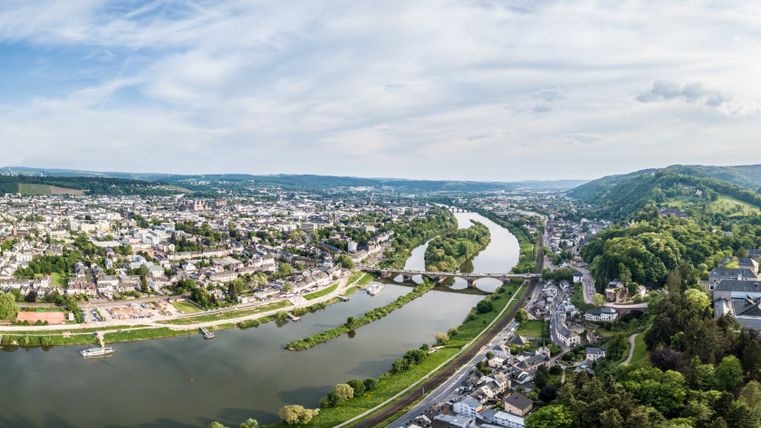Panoramablick auf Trier mit Mosel und Brücke, umgeben von grünen Hügeln.