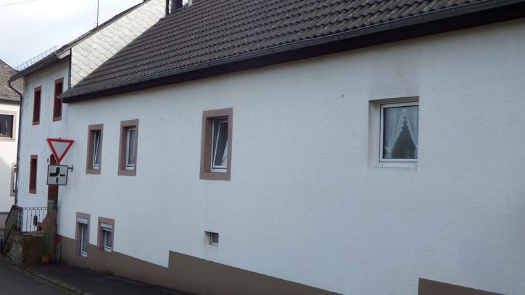 A simple residential house with a white paint and a brown base. There are several windows and a traffic sign nearby.