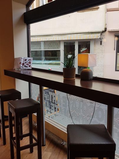 Ein gemütlicher Raum mit einer langen Fensterbank und Barhockern. Auf der Fensterbank sind einige dekorative Pflanzen und Gegenstände zu sehen.