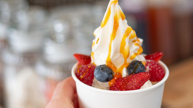 Een beker met romige Frozen Yogurt, gegarneerd met verse aardbeien, blauwe bessen en een siroop-topping. Het dessert ziet er heerlijk en verfrissend uit.