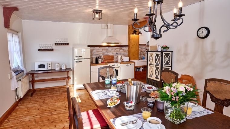 A modern kitchen with a large dining table. The table is set with breakfast items and fresh flowers.