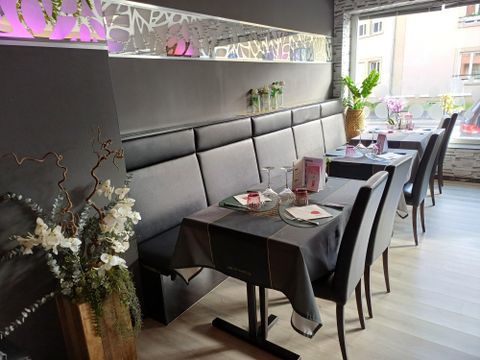 Een modern restaurant met elegante tafelkleden en decoratieve bloemen. De wanden zijn versierd en de sfeer is uitnodigend.