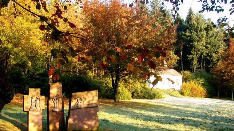 A tranquil park landscape in autumn with colorful foliage and a small white cottage. In the foreground are some interesting sculptures.