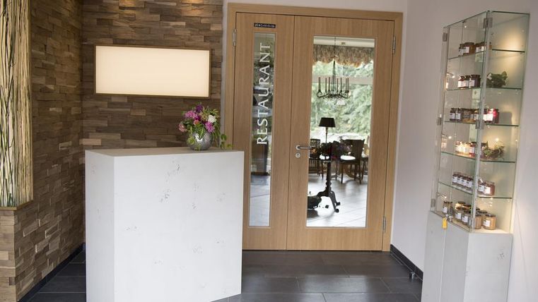 Een modern restaurant met een elegante receptiebalie van wit steen. Op de achtergrond zijn tafellakens en een decoratieve vitrine met glazen te zien.