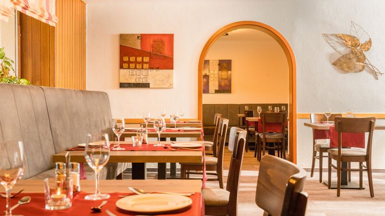 A cozy restaurant with tables and chairs in warm colors. The tables are set, and the walls are decorated with artworks.