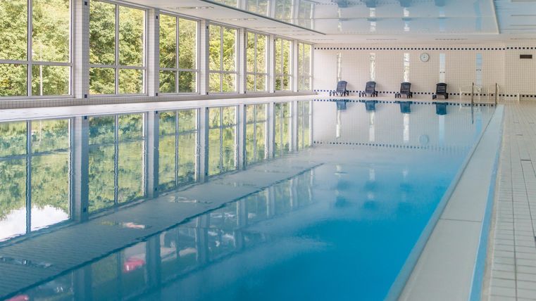 Een helder zwembad met helder water en grote ramen. De omgeving is modern en uitnodigend.