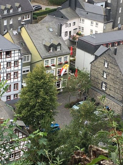 Eine malerische Stadtansicht mit traditionellen Gebäuden und einem grünen Baum im Vordergrund. Eine Fahne hängt an einem der Häuser und die Straßen sind gepflastert.
