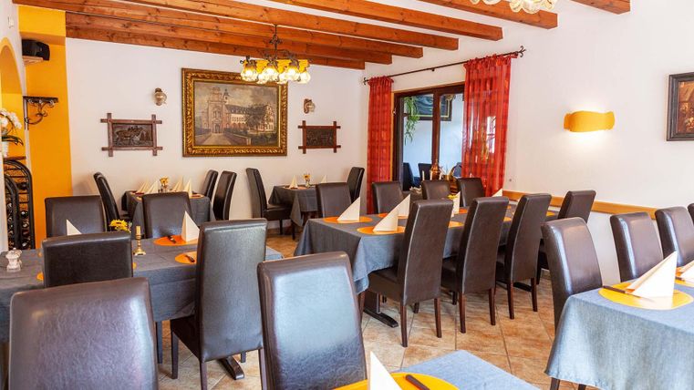 Ein gemütliches Restaurant mit Holzbalkendecke, gedeckten Tischen und braunen Stühlen. An der Wand hängt ein großes Gemälde.