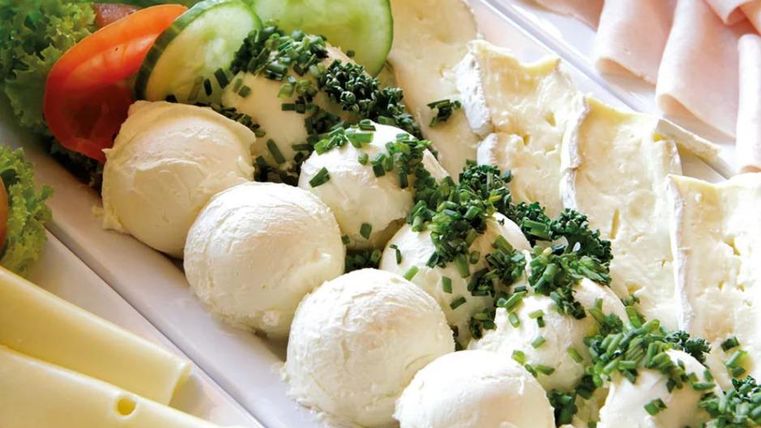 Een selectie van verschillende kaassoorten op een bord. Daaronder zijn verse kruiden, komkommers en tomaten decoratief gepresenteerd.