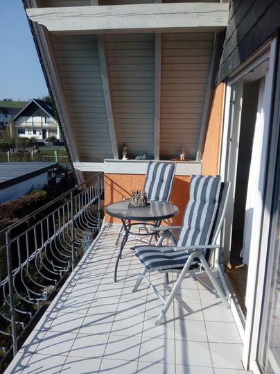 A balcony with two loungers and a small table. The sun is shining and there is a view of the surroundings.