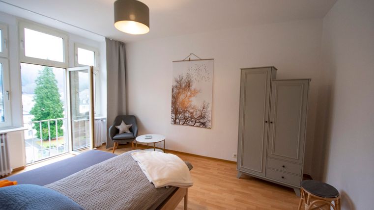 Ein modernes Schlafzimmer mit einem großen Fenster und viel Tageslicht. Es gibt ein Bett, einen Schrank und einen gemütlichen Sessel in der Ecke.