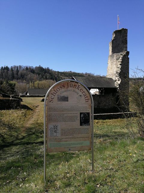 Eine Informationstafel vor der Burgruine Glaadt, mit einem hohen, alten Steinturm im Hintergrund und bewaldeten Hügeln im Hintergrund.