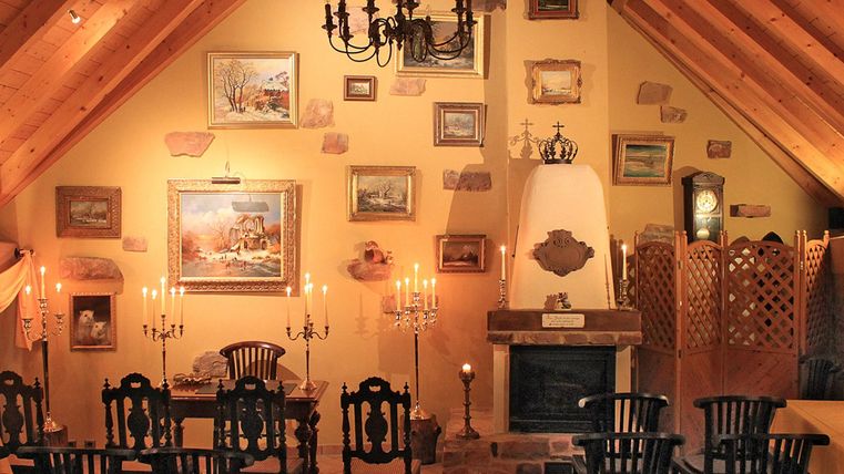 Ein gemütlicher Raum mit Holzdecke und einem großen Tisch. Wände sind mit Bildern und Kerzen dekoriert.