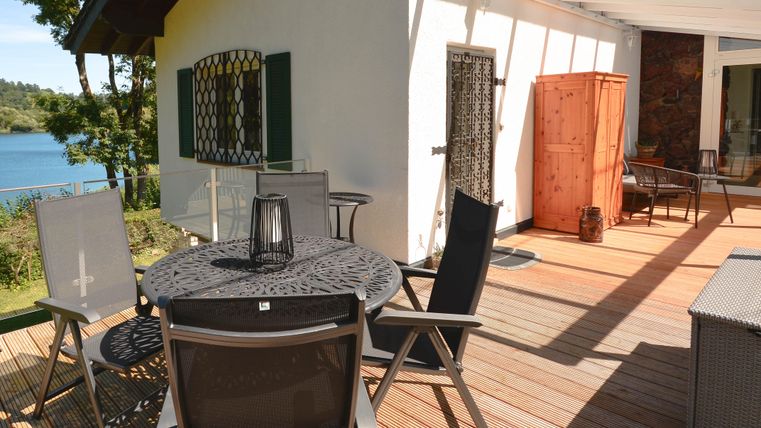 Eine helle Terrasse mit einem runden Tisch und komfortablen Stühlen. Im Hintergrund ist ein schöner Ausblick auf das Wasser zu sehen.