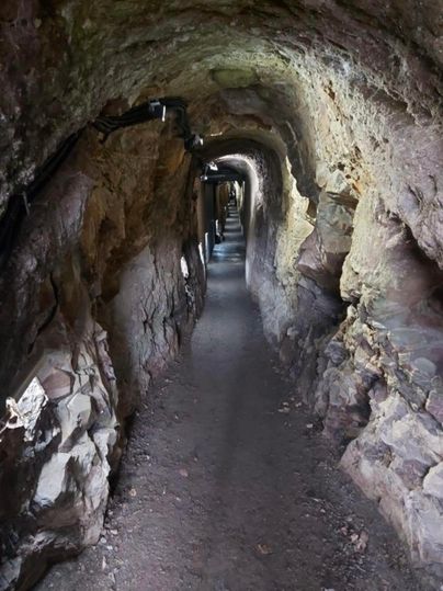 Een smalle tunnel van steen, die door zwak licht verlicht wordt. Het pad is recht en ongeveer tot halverwege zichtbaar.