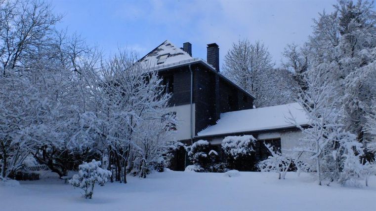 Een huis in de sneeuw, omringd door met sneeuw bedekte bomen. De lucht is blauw en helder.