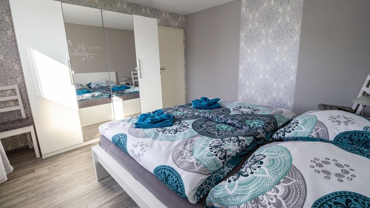 A modern bedroom with a large bed and colorful bedding. The room has a large mirror and bright walls that create an inviting atmosphere.