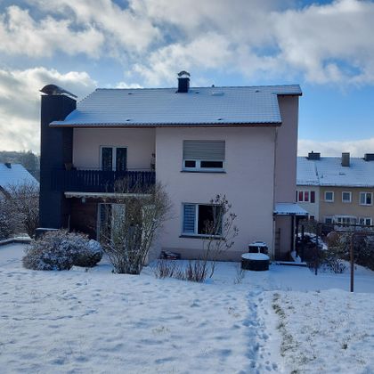 Ein Haus im Schnee mit einem kleinen Garten. Der Himmel ist blau mit einigen Wolken.