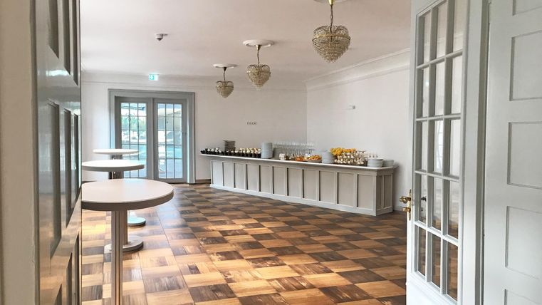 Een lichte, moderne kamer met een houten vloer. Op een lange console staan verschillende gerechten en dranken klaar.