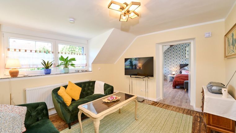 A cozy living room with a green sofa and a table. The room has large windows and is brightly lit.