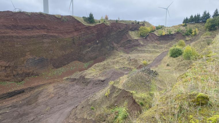 Hier hat man einen Ausblick auf den Vulkan. Man sicht leicht bewachsene Hügel. Der Himmel ist bewölkt.