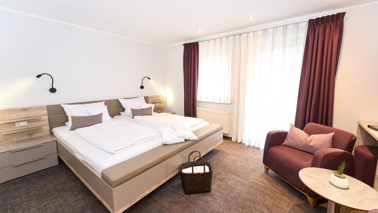 Een modern hotelkamer met een groot tweepersoonsbed en een gezellige stoel. Er zijn veel ramen die zorgen voor daglicht, en een stijlvolle decoratie.