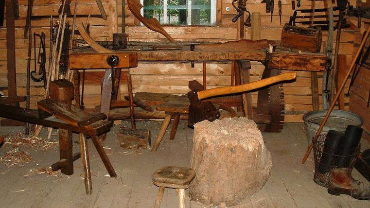 Eine traditionelle Tischlerei mit verschiedenen Werkzeugen und Holzarbeiten. Der Raum ist rustikal und aus Holz, mit einer Werkbank in der Mitte.