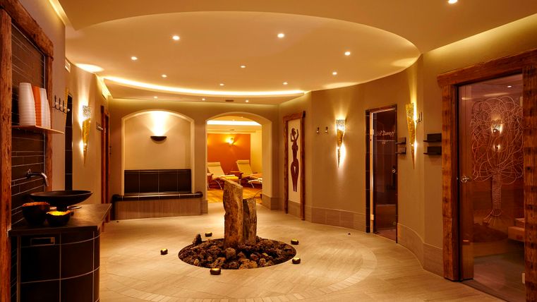 An elegant wellness area with soft lighting and a central stone element. The walls are painted in warm tones, creating a relaxing atmosphere.