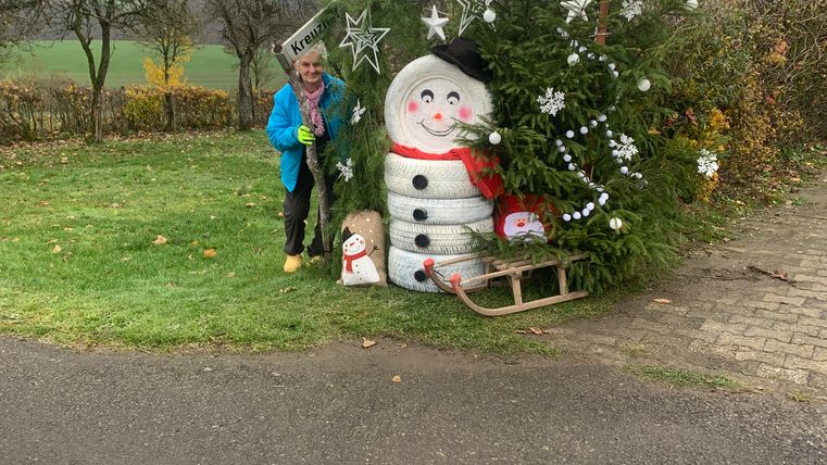 Ein Weihnachtsmann, der aus einem Baum geformt ist, steht in einer grünen Wiese. Daneben steht eine Person in blauer Jacke.
