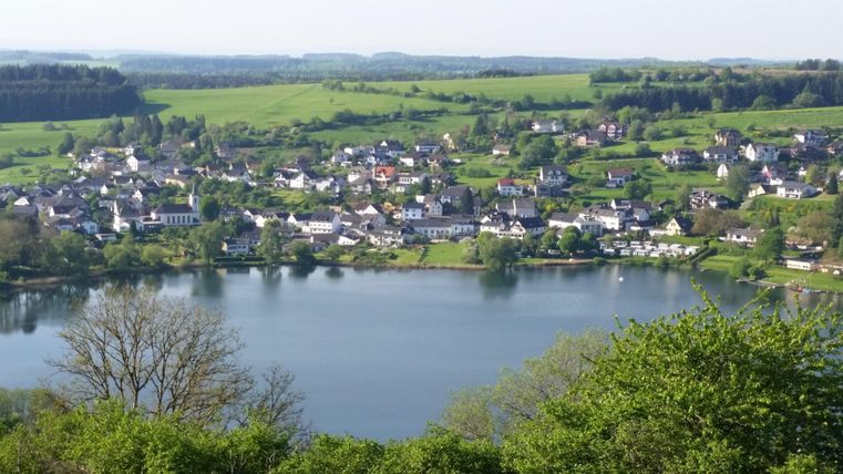 Eine malerische Landschaft mit einem See und einer kleinen Stadt am Ufer. Die Umgebung ist grün und hügelig, ideal für Erholung in der Natur.