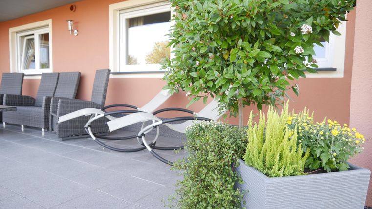 A cozy outdoor area overlooking a terrace. There are comfortable chairs, plants, and a beautifully designed flower box.