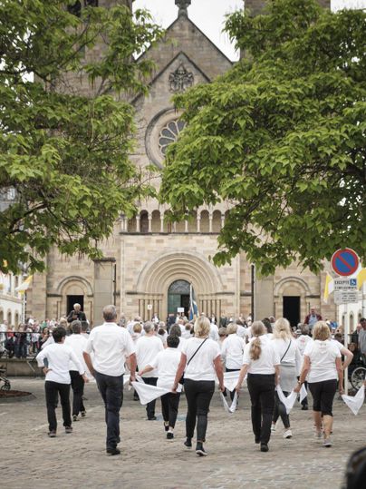 Een grote menigte verzamelt zich op een plein. Een parade met muzikanten in rode en witte uniformen trekt voorbij.