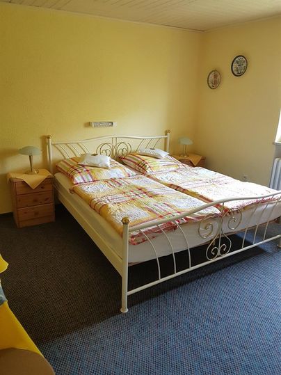 Ein gemütliches Schlafzimmer mit einem Doppelbett und gelben Wänden. Auf dem Nachttisch stehen zwei Lampen und es gibt bunte Bettwäsche.