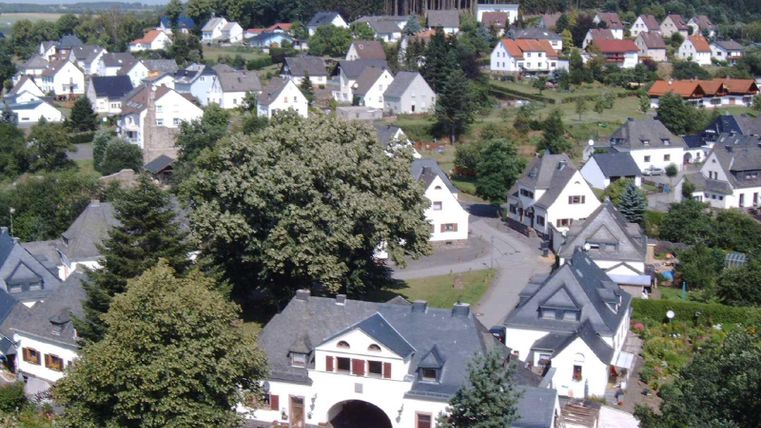 Blick von oben auf die Eisenbahnseidlung "Neue Kolonie". Eine in den  1920 Jahren entstandene Wohnanlage für Eisenbahnbedienstete gruppiert sich in der Form eines Dreiecks, in dessen Mitte ein
großer Laubbaum steht.Sie besteht aus Torhaus, sechs Doppelhäusern und einem eingeschossigen Riegel mit sechs Wohneinheiten. Im Hintergrund stehen viele Häuser aus verschiednen Bauphasen.