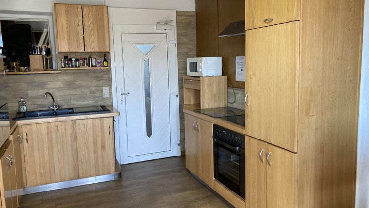 A modern kitchen with wooden furniture and a bright, inviting space. The amenities include a cooktop, an oven, and a microwave.