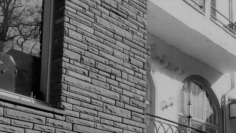 Eine alte Gebäudeansicht mit einer Ziegelwand und einem Schaufenster. Ein Schild zeigt den Namen des Geschäfts an.