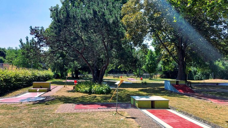 A quiet mini-golf course with numerous lanes and well-maintained grass. Trees and shrubs surround the play area, creating a pleasant atmosphere.