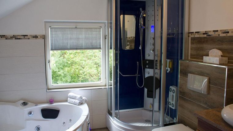 Ein modernes Badezimmer mit einer Dusche und einer Whirlpool-Badewanne. Durch das Fenster sieht man grünes Laubwerk.