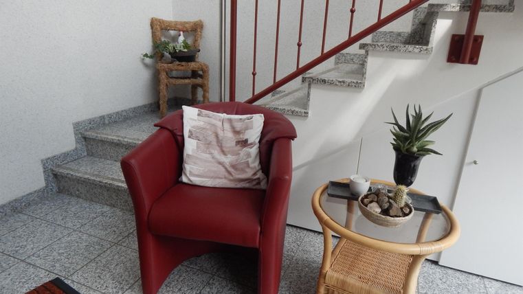 A red armchair is next to a table with a plant. Stairs are visible in the background.