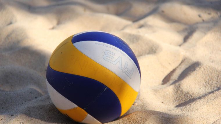 A blue, yellow, and white striped volleyball lies on a sandy surface.